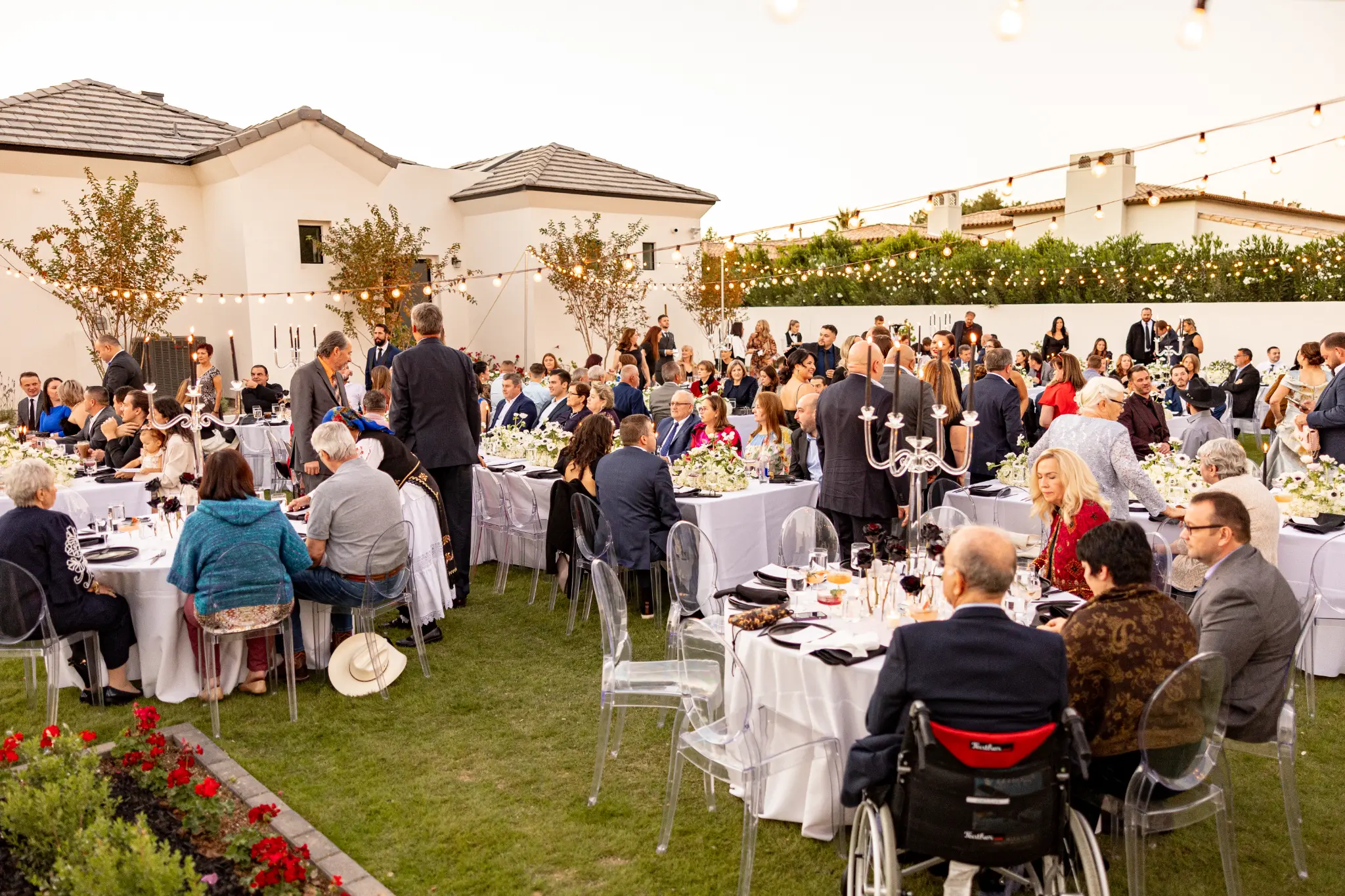 Wedding reception guests dining under string lights in a lush garden