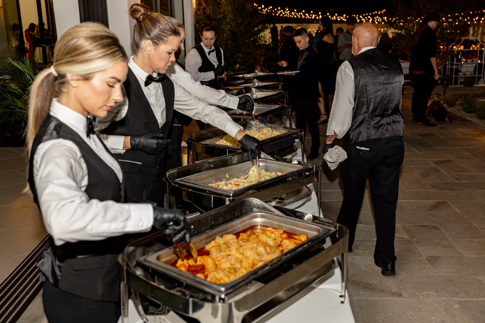 Catering staff serving a wedding buffet line at an outdoor evening event